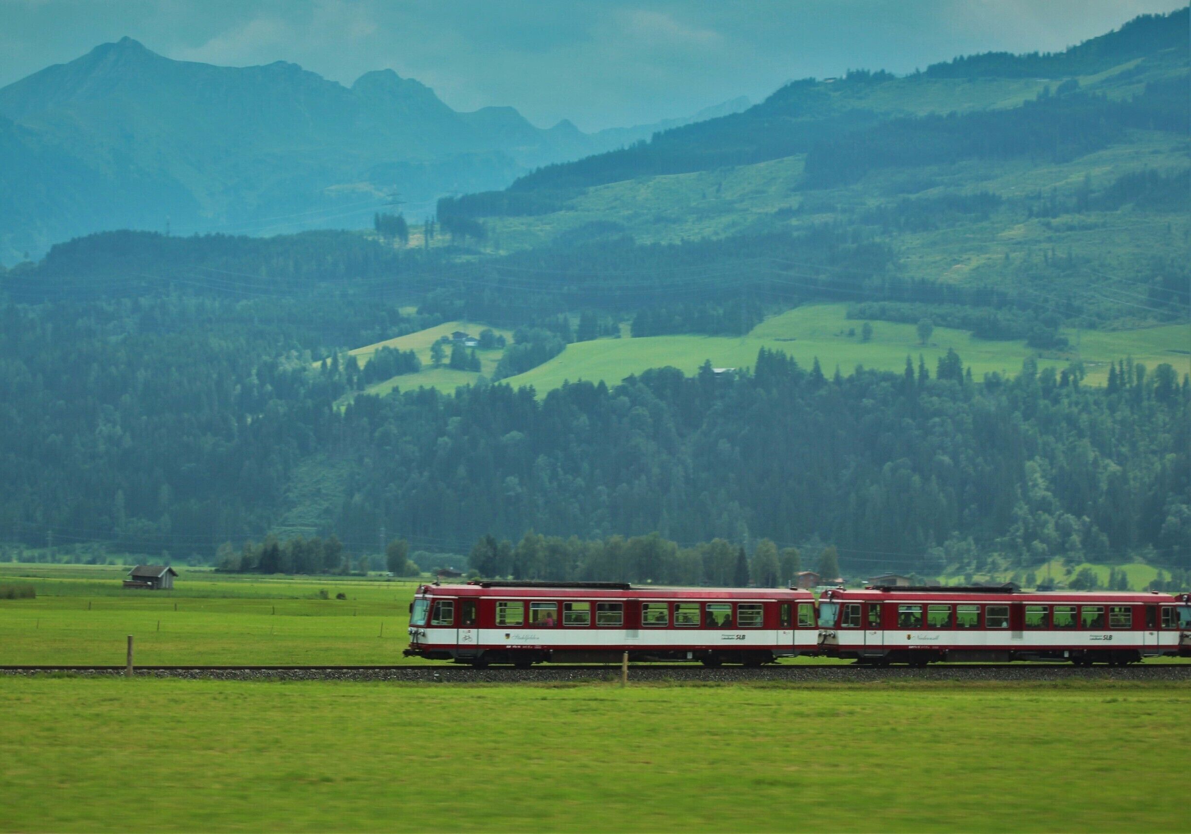 A red and white train traveling through a green valley with mountains in the background.