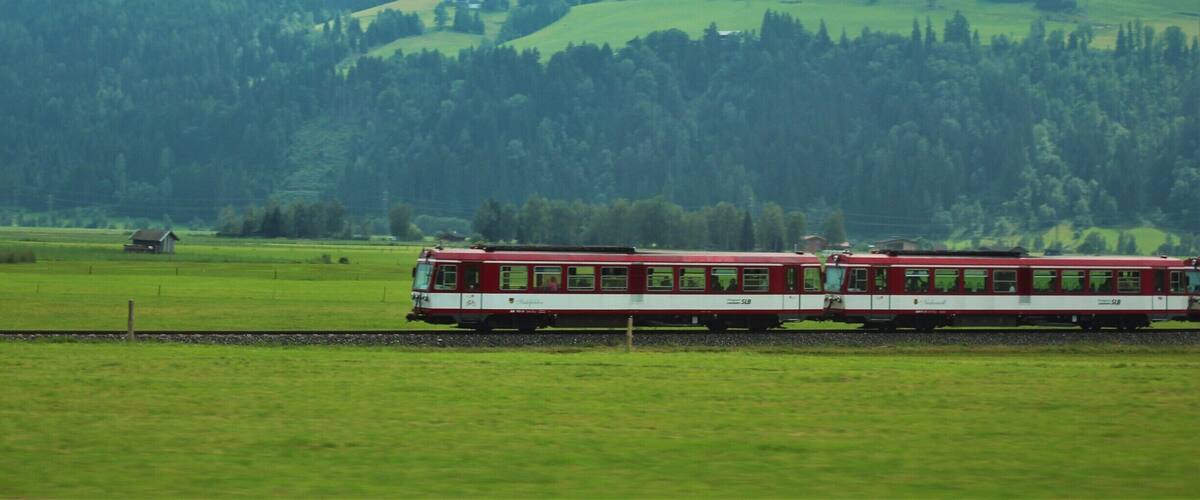 A red and white train traveling through a green valley with mountains in the background.