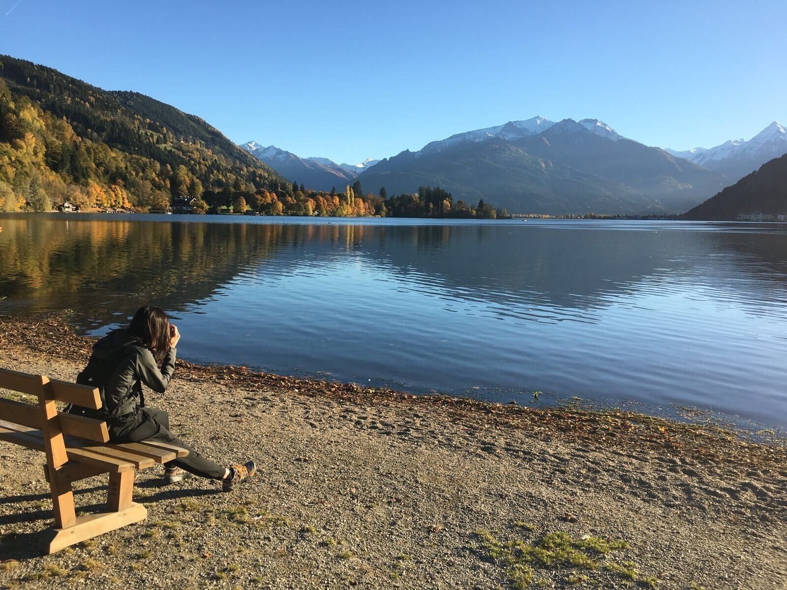 A person sitting on a bench by a calm lake with mountains in the background.