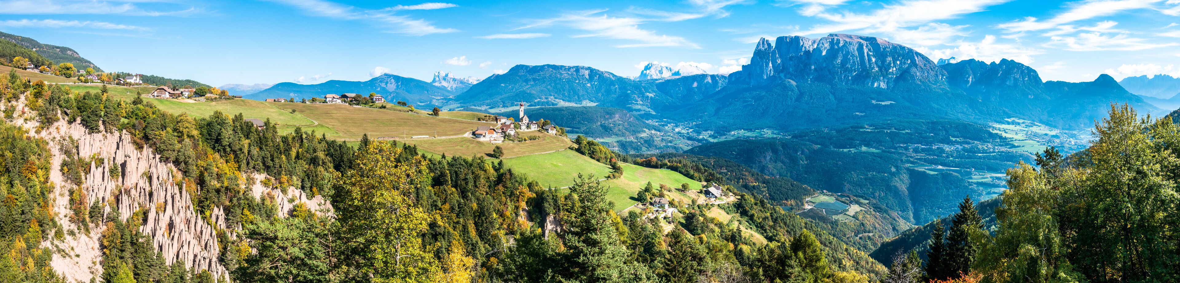 A mountainous landscape with a village, forested areas, and a prominent mountain peak.