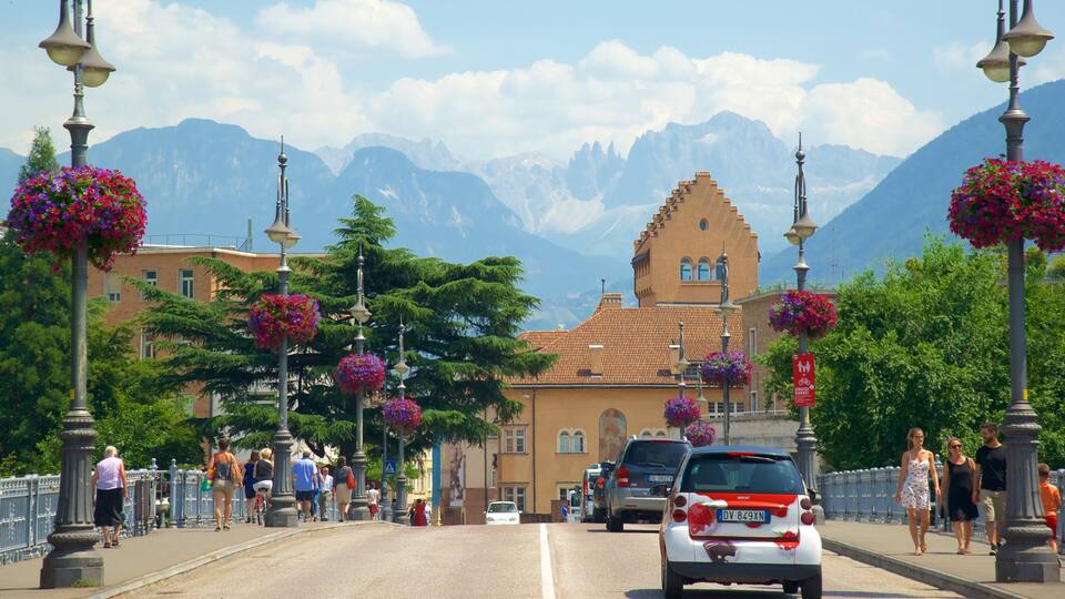 A bridge with flower baskets, a building with a tower, and mountains in the background.