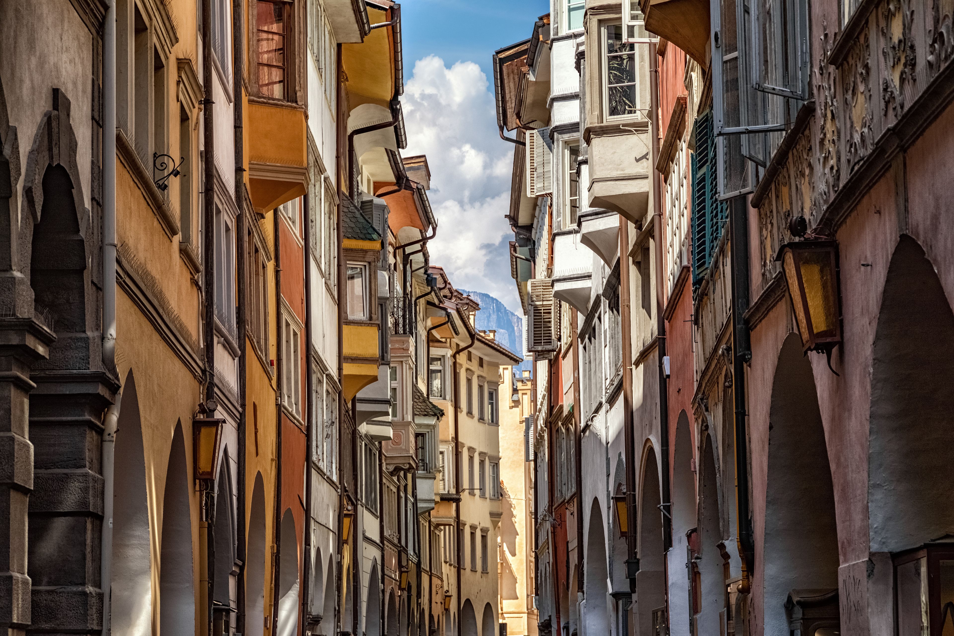 A narrow street lined with historic buildings, featuring arched doorways and ornate facades.