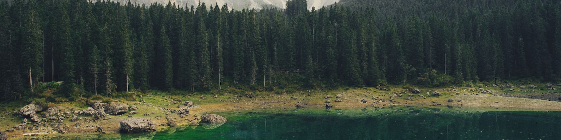 Una pareja en un afloramiento rocoso con vistas a un lago cristalino y montañas al fondo.