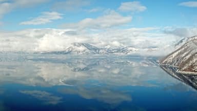 Um lago tranquilo refletindo montanhas cobertas de neve e um céu límpido.