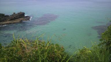 A coastal landscape with clear turquoise waters, rocky outcrops, and distant mountains.