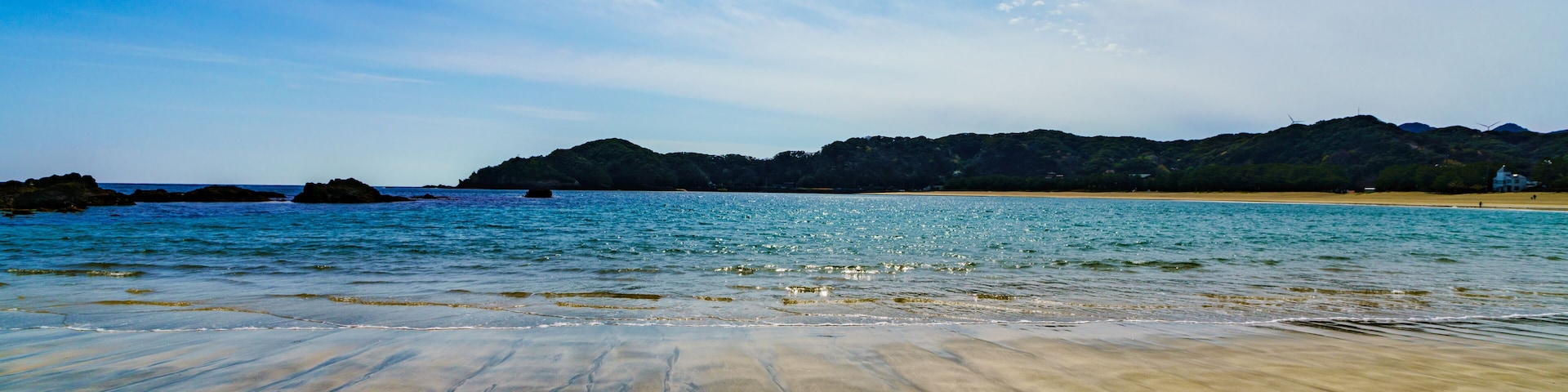A beach with clear water, sandy shore, and distant hills.