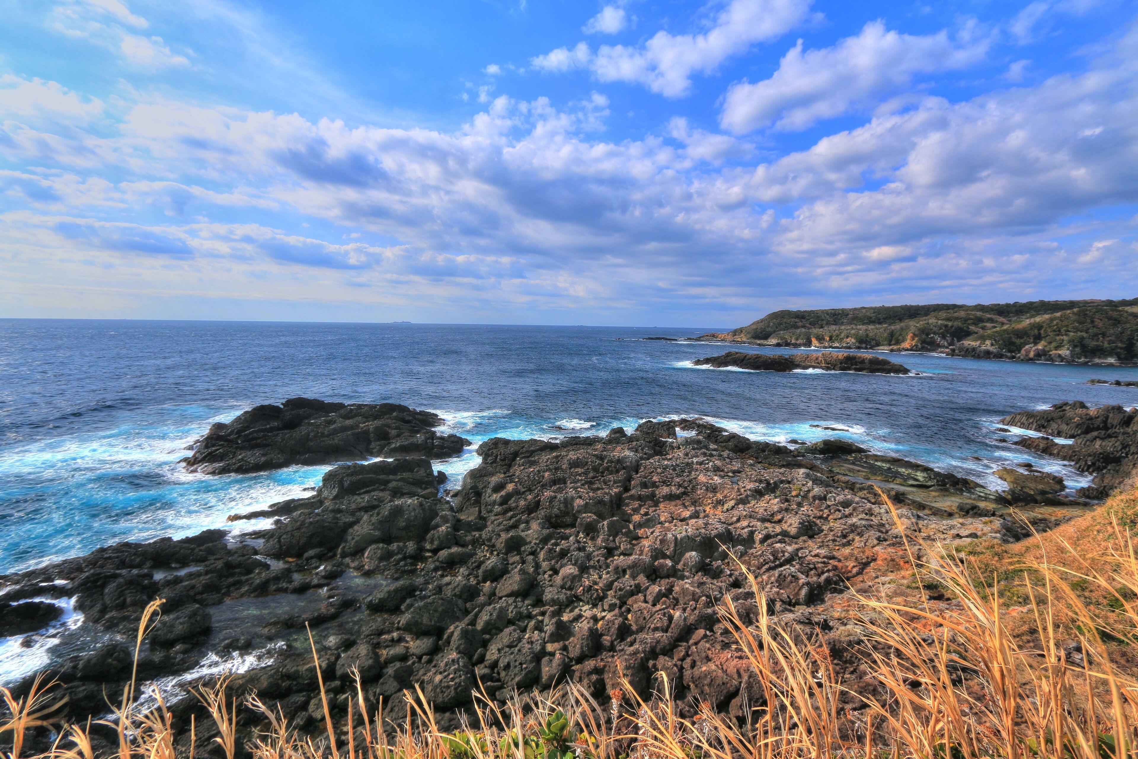 A coastal landscape with rocky terrain, ocean waves, and a clear sky.