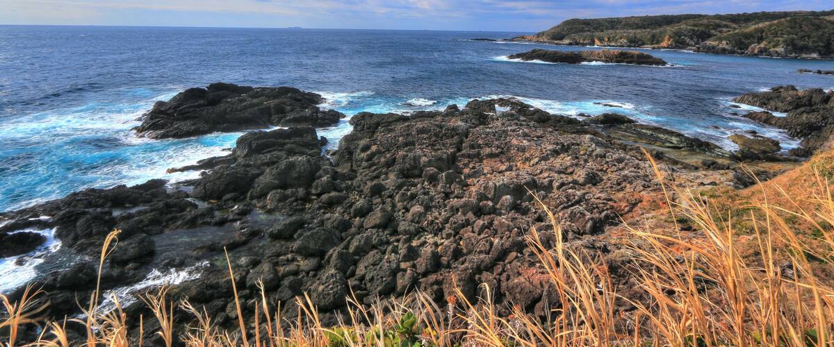 A coastal landscape with rocky terrain, ocean waves, and a clear sky.