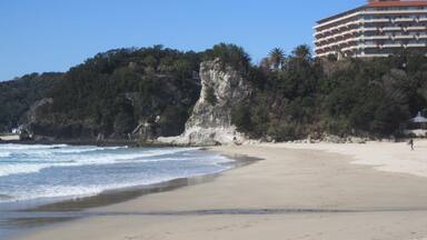 A beach with a rocky cliff and a building in the background.