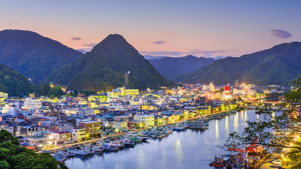 A coastal town with a river, boats, and mountains in the background.