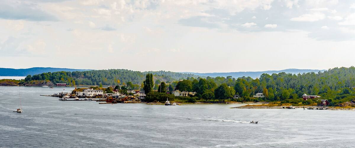 A coastal town with boats, a lighthouse, and a forested hill in the background.