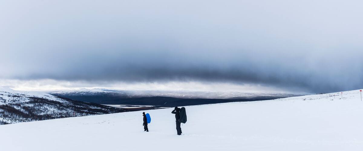 A snowy mountain landscape with two people carrying backpacks.