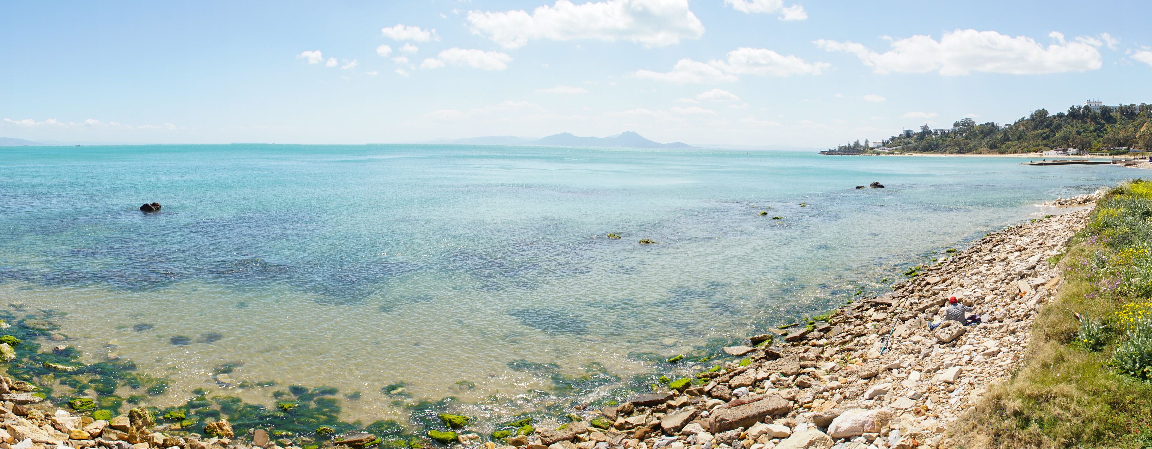A clear turquoise sea with rocky shorelines and distant mountains.