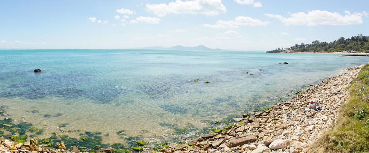 A clear turquoise sea with rocky shorelines and distant mountains.