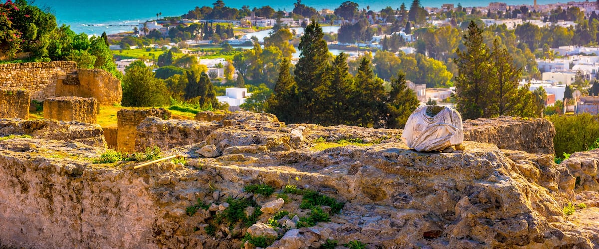 Des ruines antiques, une ville côtière et une montagne en arrière-plan.