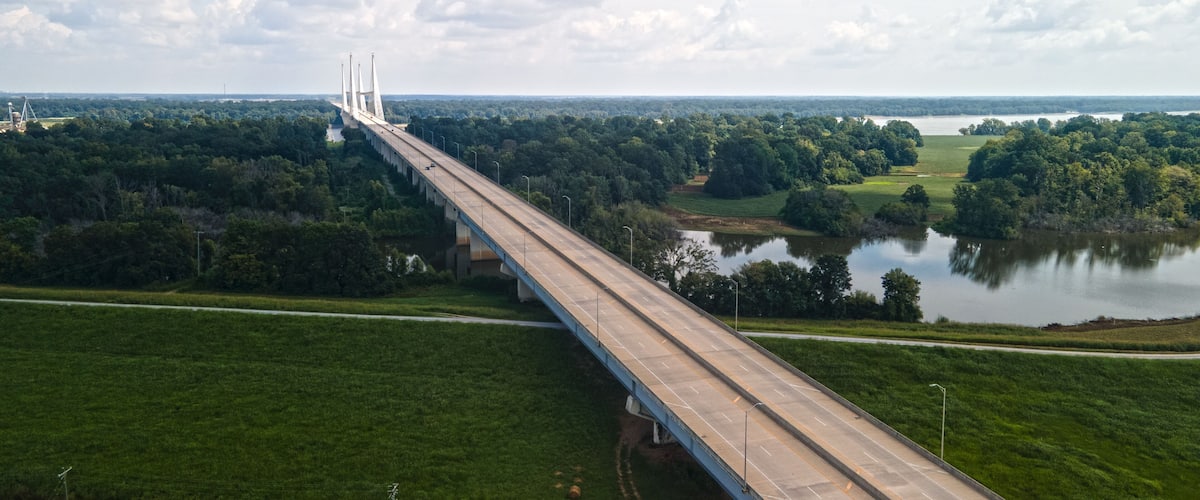 A long bridge spanning a river with a forested landscape on either side.