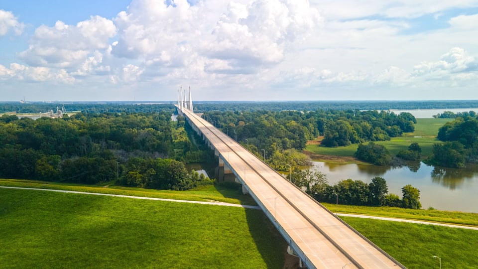 A long bridge spanning a river, surrounded by lush greenery and fields.