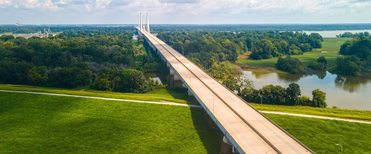 A long bridge spanning a river, surrounded by lush greenery and fields.