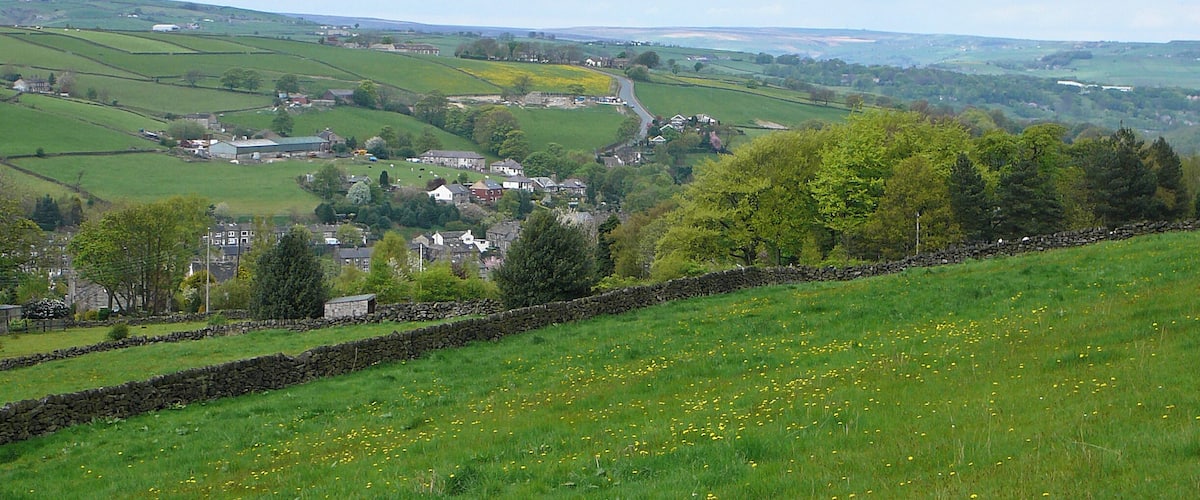 A rural landscape with rolling hills, a stone wall, and scattered houses.