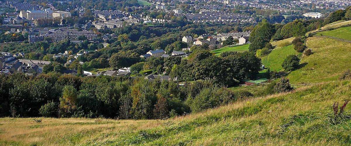 A panoramic view of a town with rolling hills, dense residential areas, and a prominent tower in the distance.