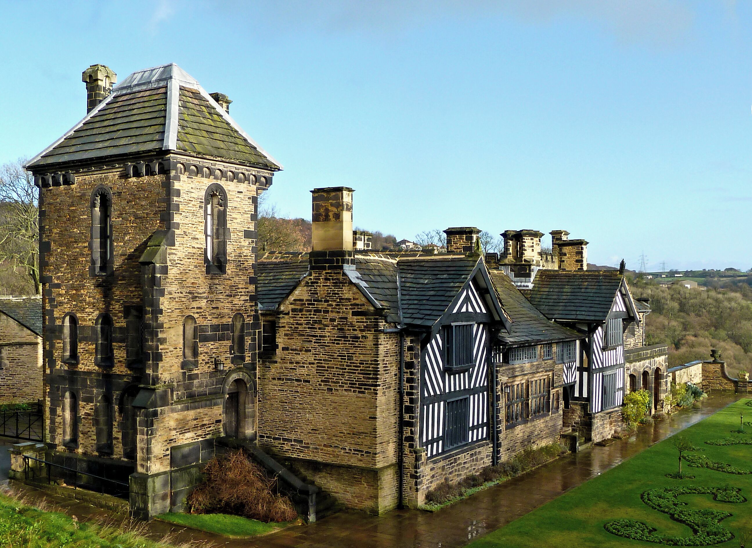A historic stone building with a tower, surrounded by a moat and a well-maintained garden.