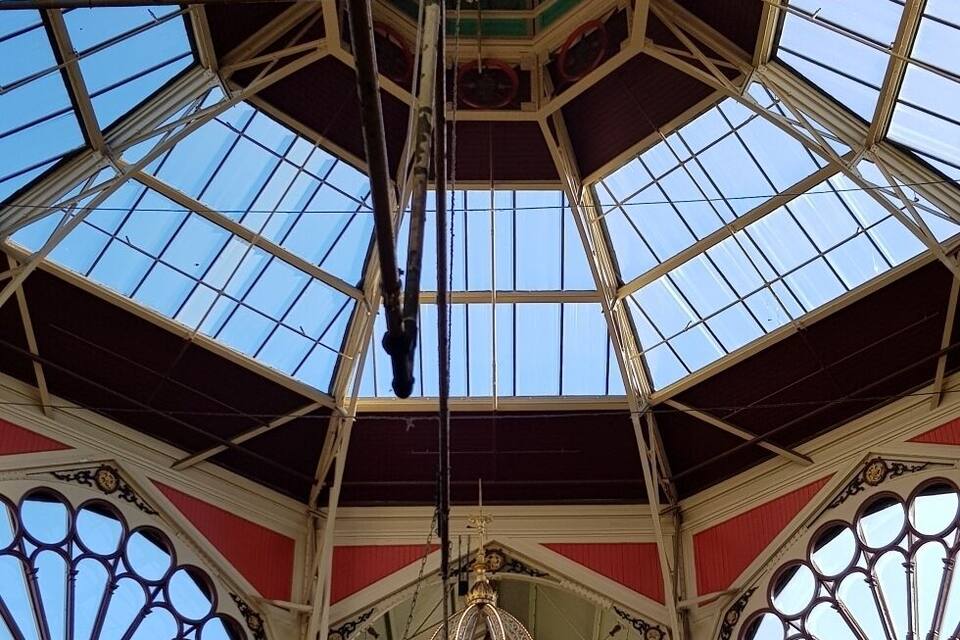 Un reloj grande y ornamentado cuelga del techo de un mercado con techo de cristal.