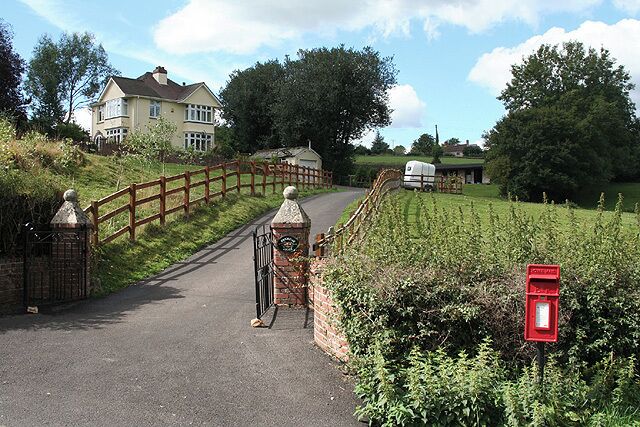 A rural road with a wooden bridge, a mailbox, and a house in the background.