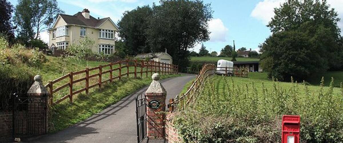 A rural road with a wooden bridge, a mailbox, and a house in the background.