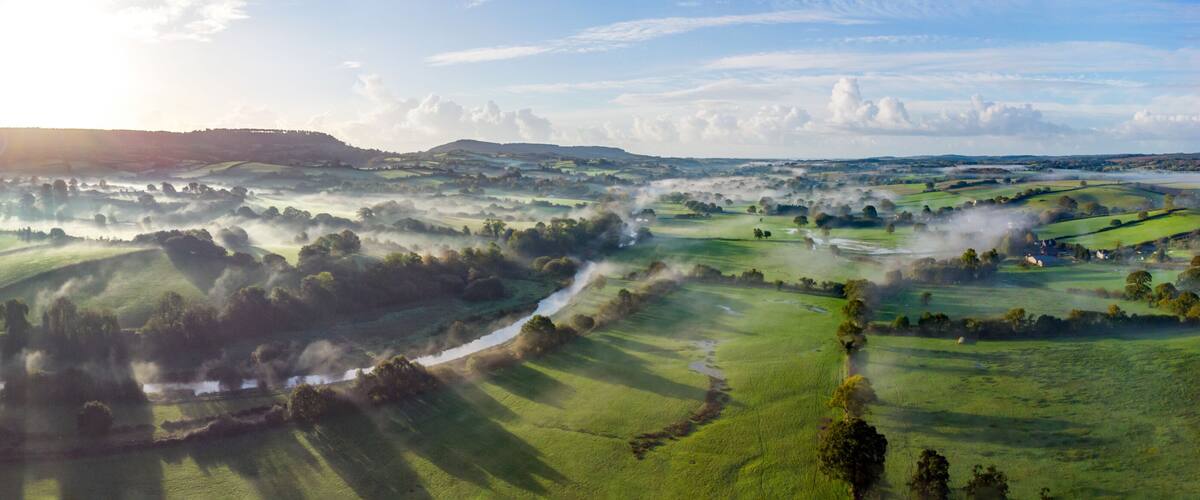 Rolling green hills, a river, and a distant village.