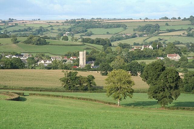 Rolling green hills, a church tower, and scattered houses in a rural landscape.