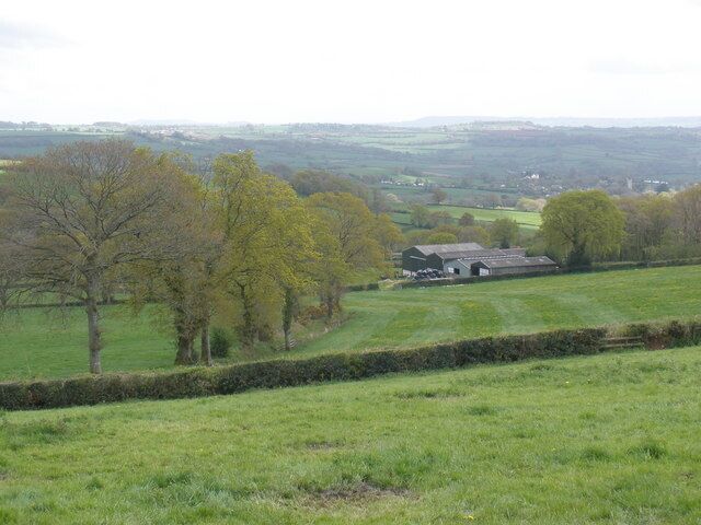 A rural landscape with a barn, trees, and rolling hills in the background.