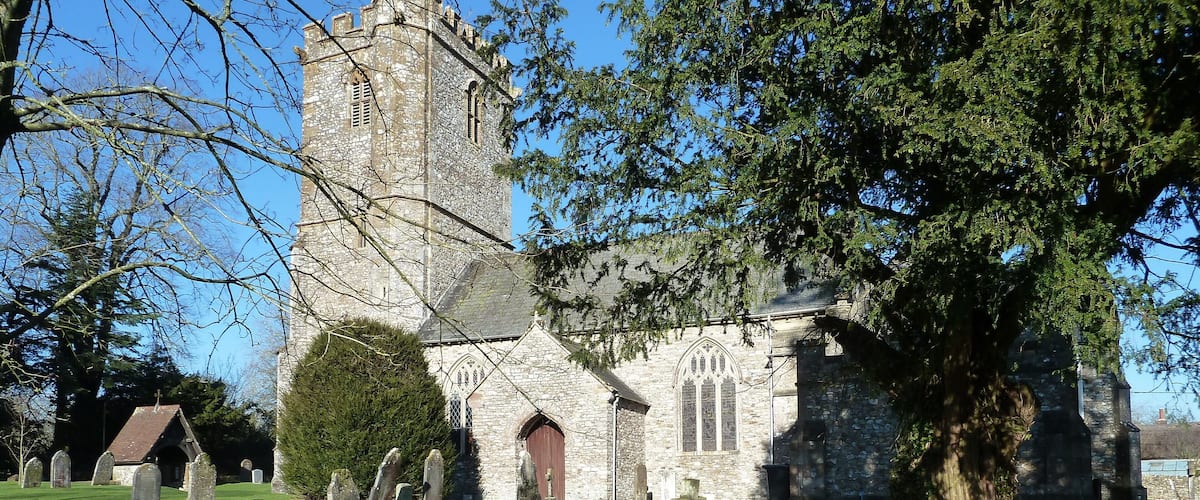 A stone church with a tower, surrounded by a cemetery with headstones.