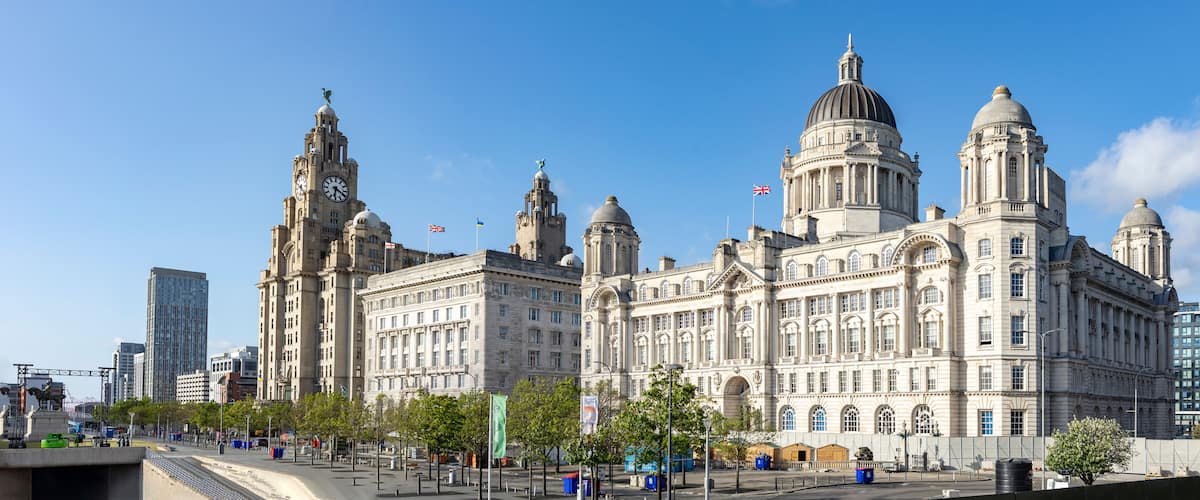 A historic building with multiple domes and towers, surrounded by modern skyscrapers and a clear blue sky.