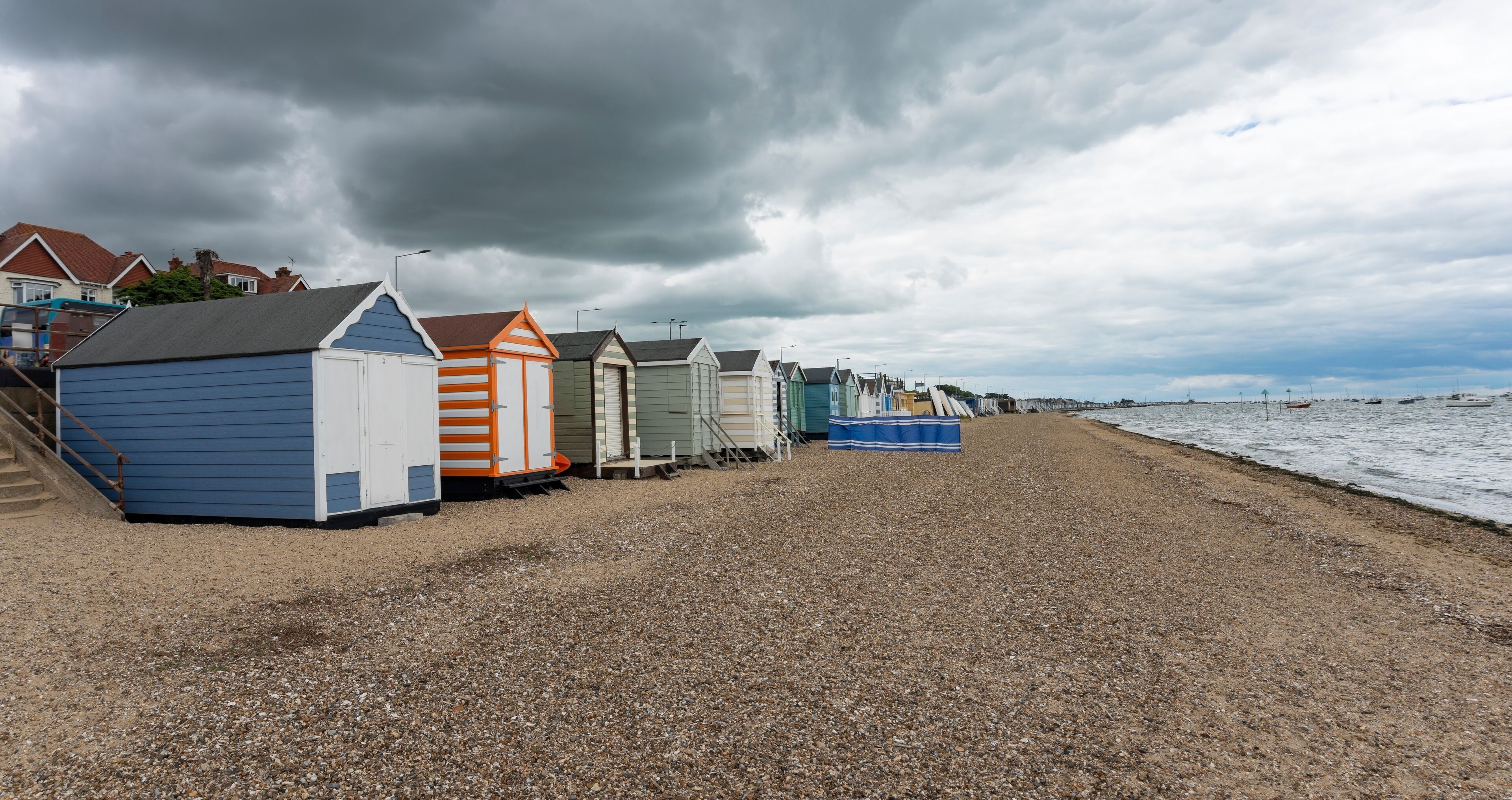 A row of beach huts along a pebbled beach with a stormy sky.