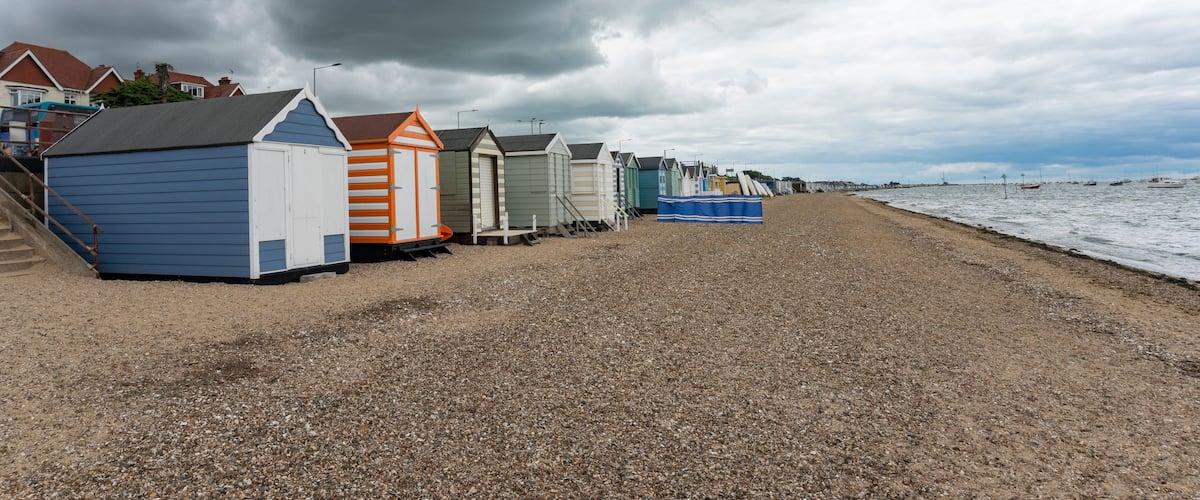 A row of beach huts along a pebbled beach with a stormy sky.