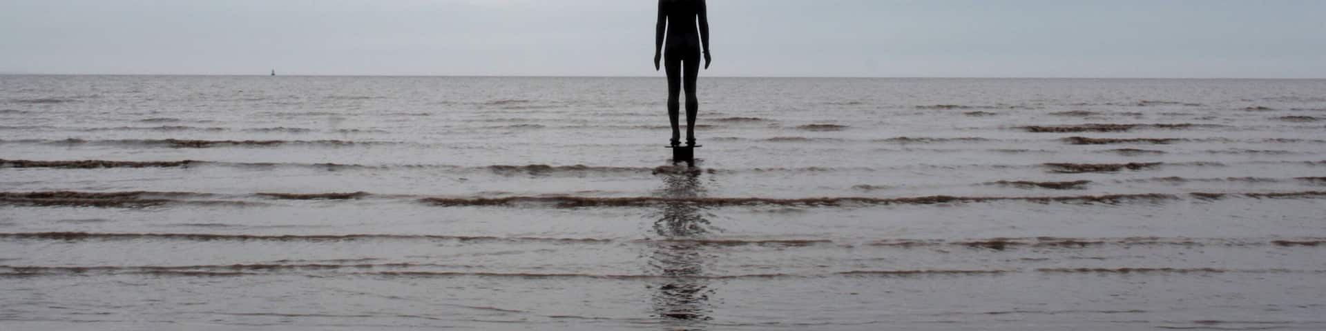 A person standing in shallow water with a cloudy sky.
