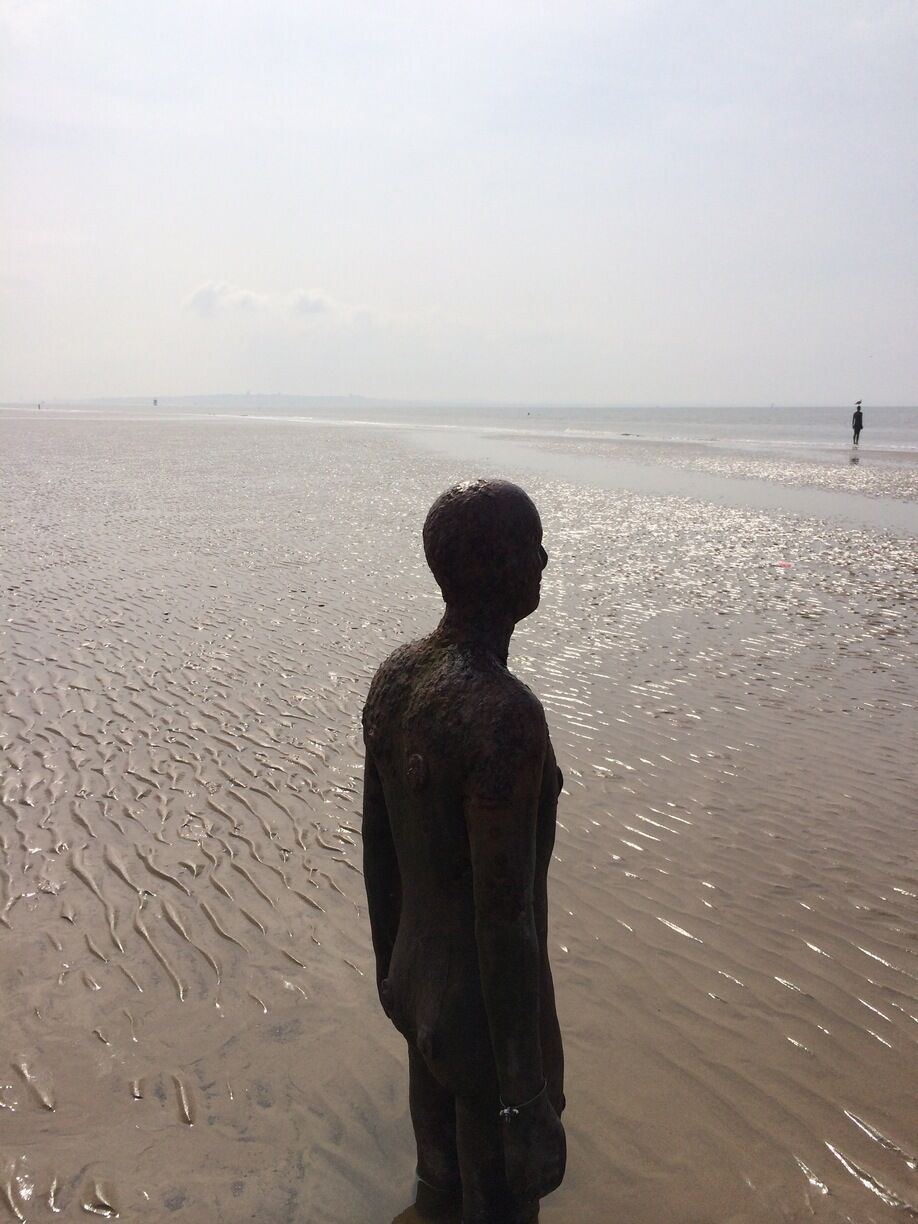 A person standing on a sandy beach with a calm sea in the background.
