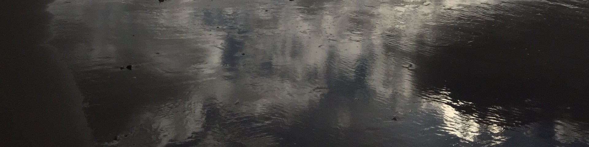 Una playa con arena mojada y nubes dispersas en el cielo.