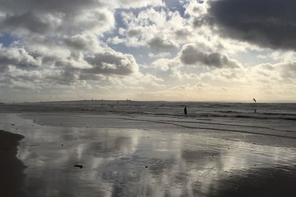 Uma praia com areia molhada e nuvens esparsas no céu.