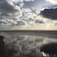 A beach with wet sand and scattered clouds in the sky.