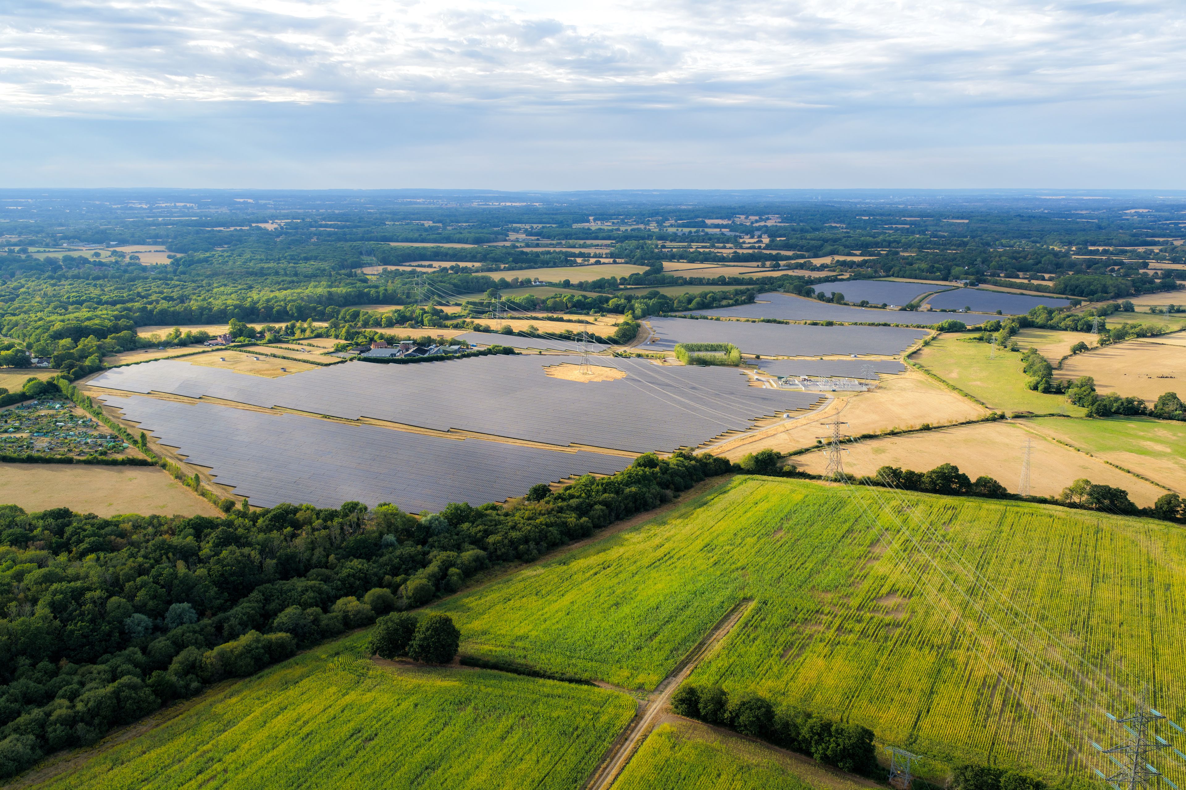 A large solar farm with multiple rows of solar panels, surrounded by green fields and a lake.
