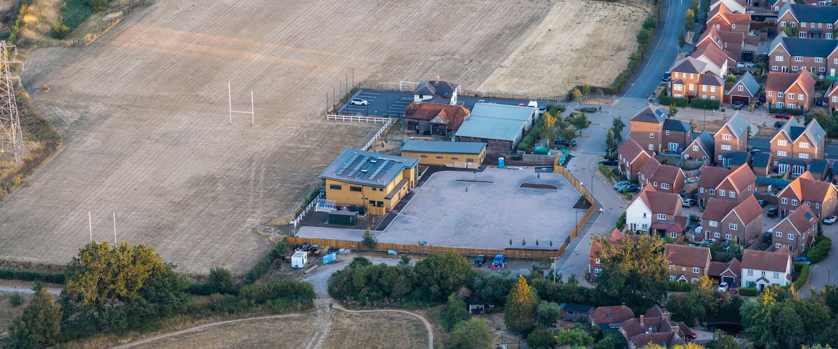 An aerial view of a residential area with houses, a large open field, and a solar panel installation.
