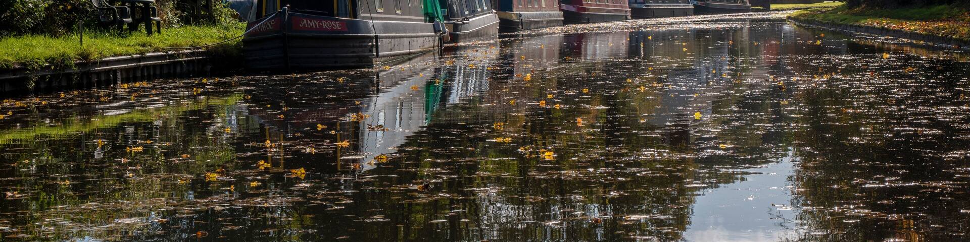 a row of narrow boats on one of Dudley's many canals (or the cut as we know it) near the Stewponey in Stourton. with autumn colours in the trees and still reflective water bellow