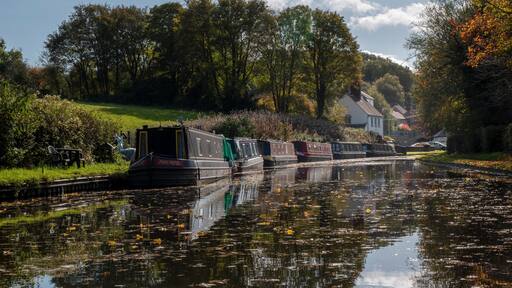 a row of narrow boats on one of Dudley's many canals (or the cut as we know it) near the Stewponey in Stourton. with autumn colours in the trees and still reflective water bellow