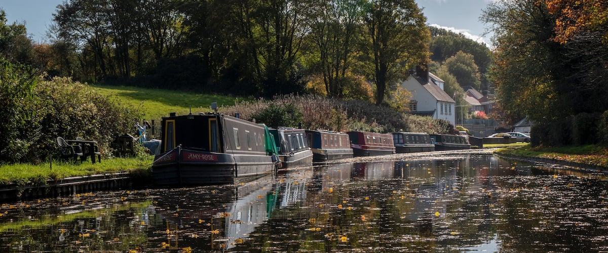 A canal with narrowboats, surrounded by trees and houses.
