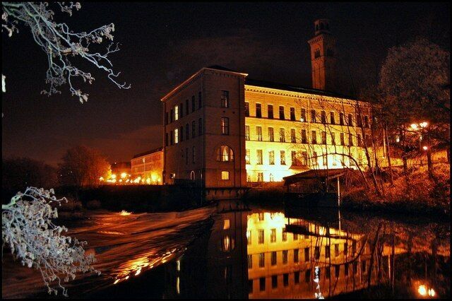 A historic building with a tower, illuminated by warm lights, reflecting on a calm body of water.