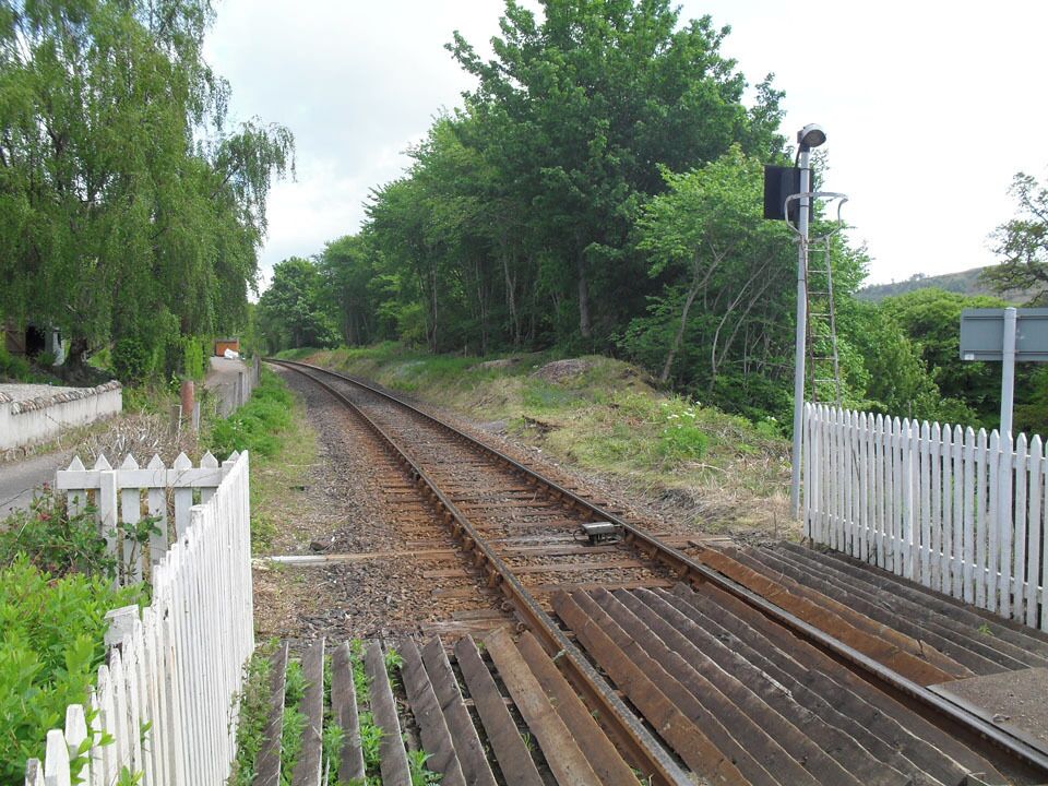 A railway track with a white fence on one side and trees on the other.
