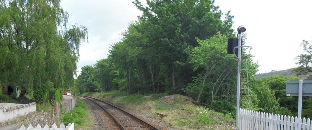 A railway track with a white fence on one side and trees on the other.