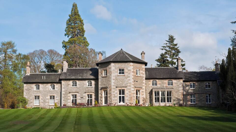 A large stone building with a central tower, surrounded by a well-manicured lawn and tall trees.