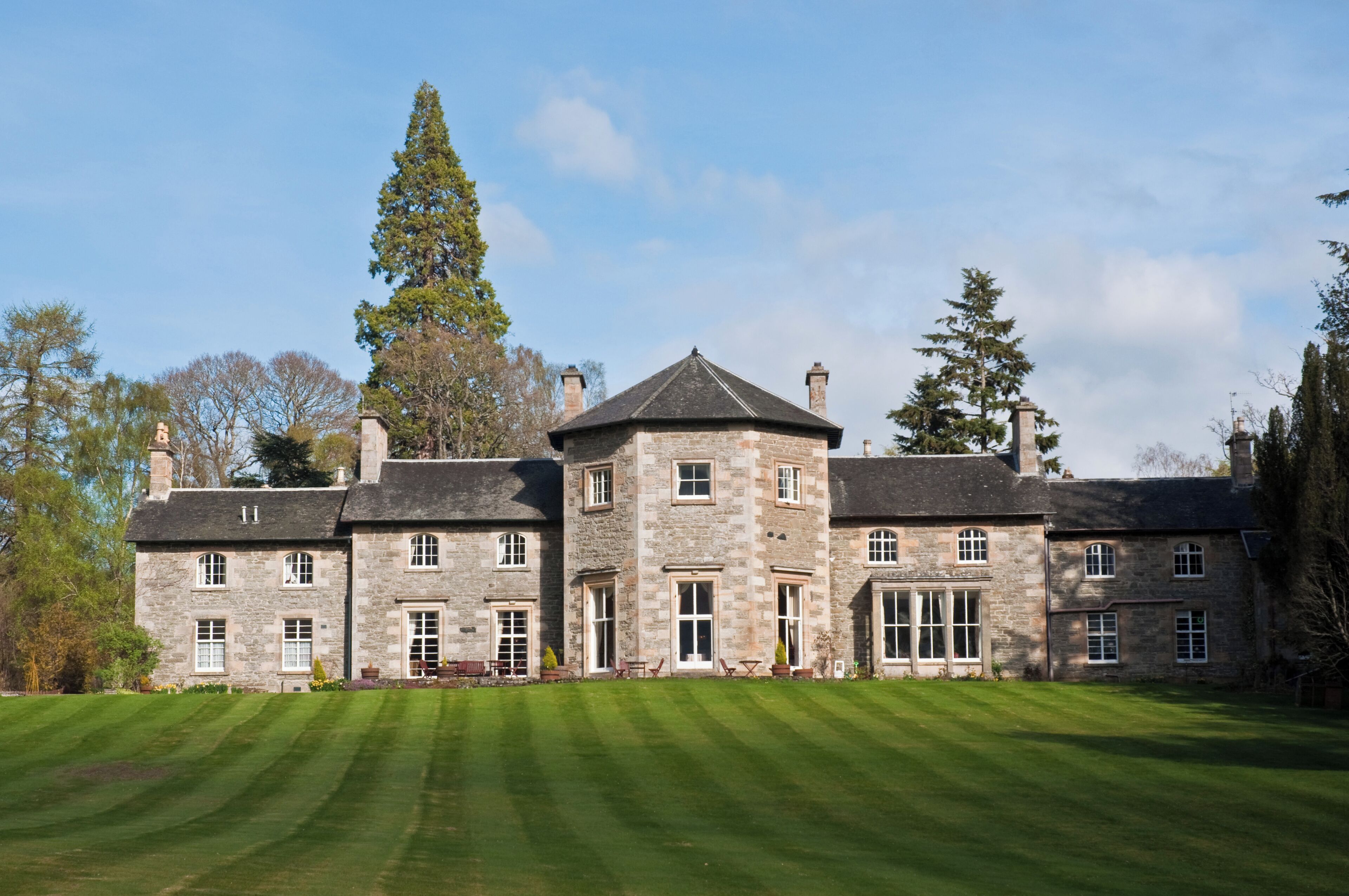 A large stone building with a central tower, surrounded by a well-manicured lawn and tall trees.